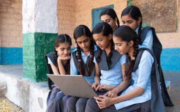 Group of rural school girls in uniform sitting in school corridor working on laptop - concept of digital education